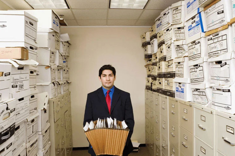 Man carrying files in his hands inside an office filled with storage boxes